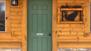 Puinen mökki, jossa on vihreä ovi, tupakointikieltokyltti ja oven yläpuolella kyltti, jossa lukee ”MUSKY LODGE”.
