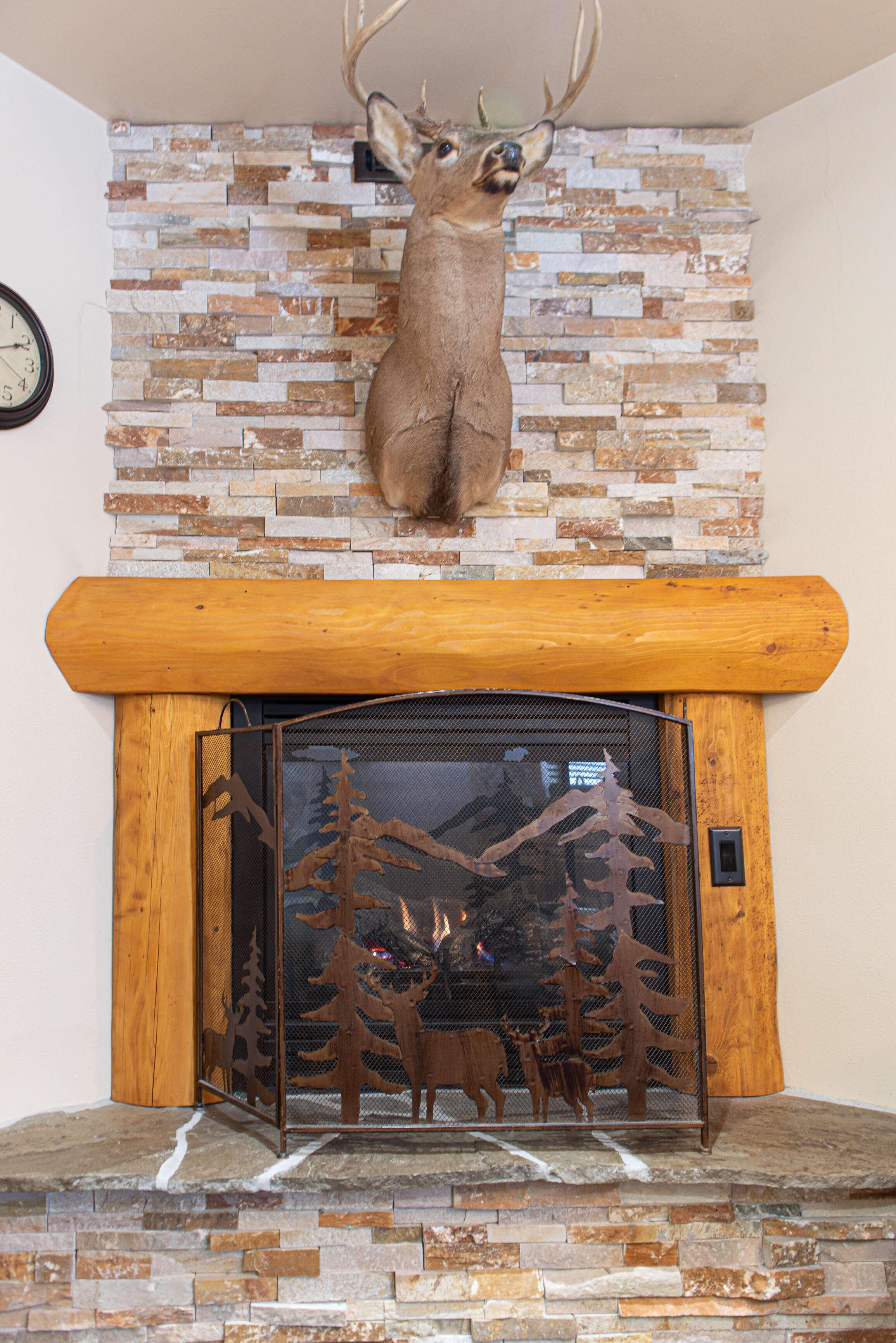 Une cheminée surmontée d’une tête de cerf, un mur en pierre et une étagère en bois.