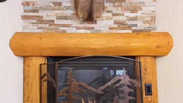 Une cheminée surmontée d’une tête de cerf, un mur en pierre et une étagère en bois.