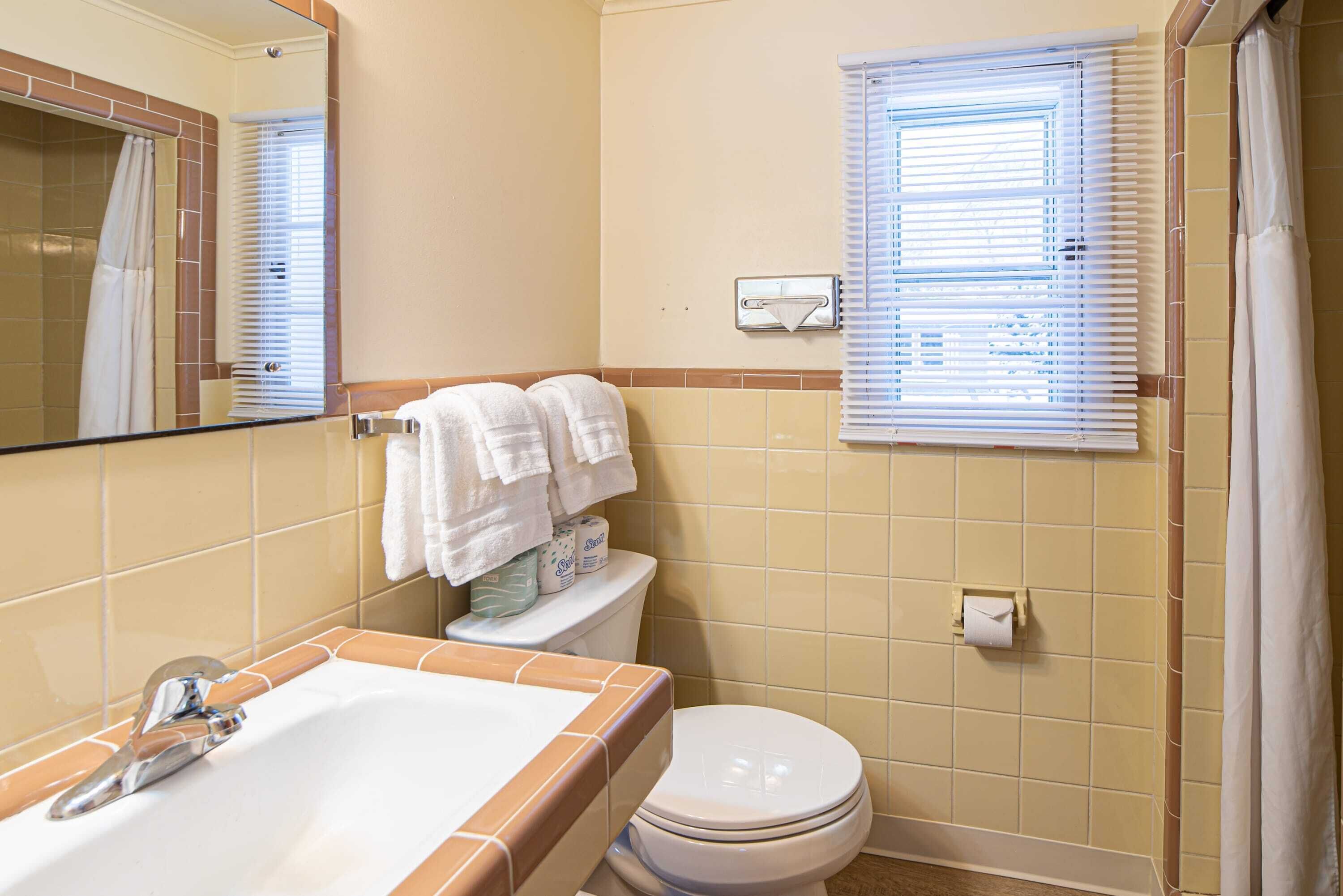 Un baño con bañera, inodoro y ventana con persianas.