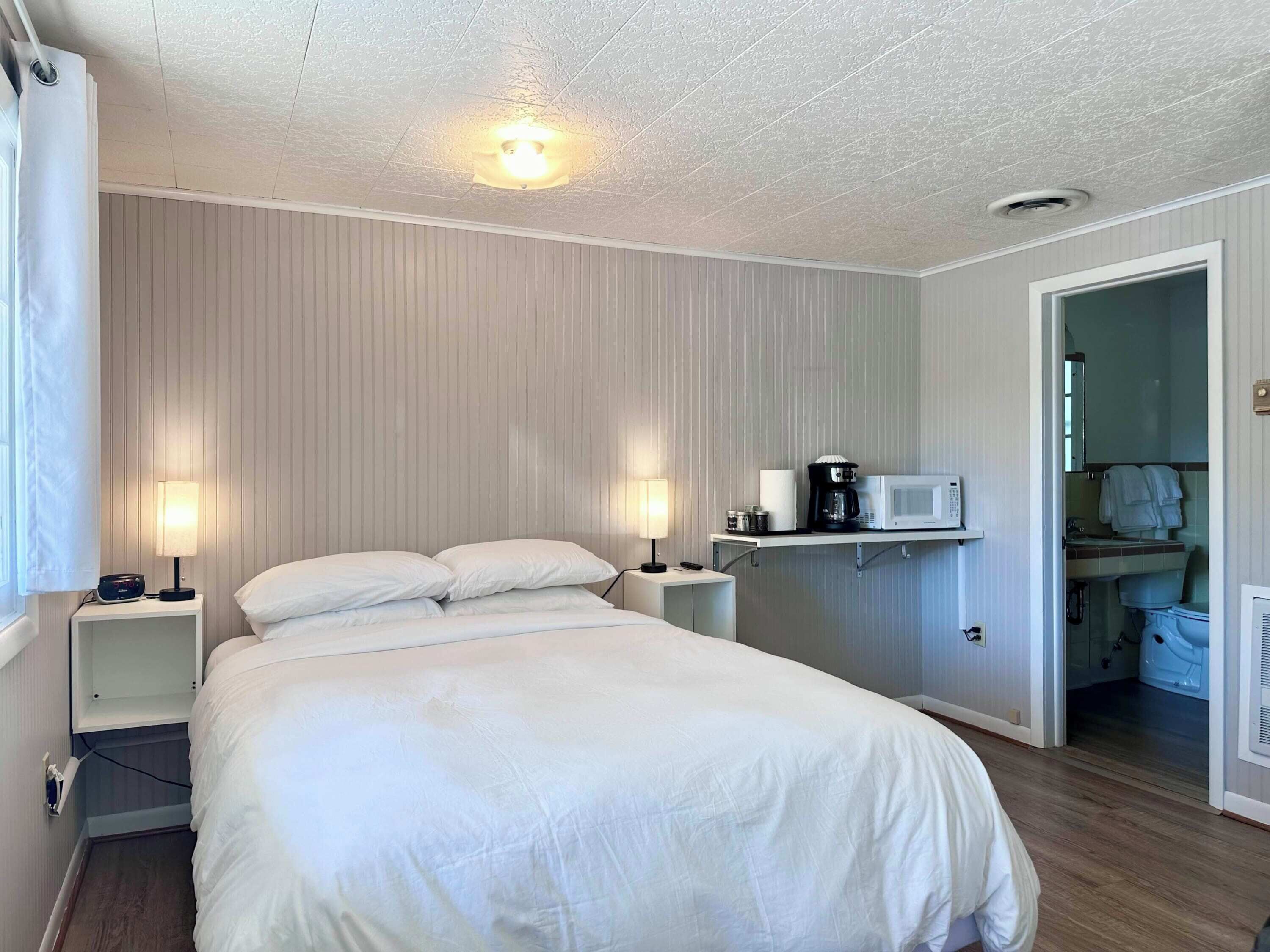 A hotel room with a large bed, bedside lamps, a microwave, and a small table.