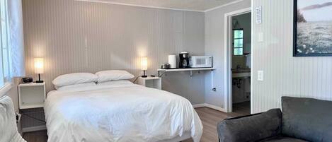 A hotel room with a bed, bedside tables, a chair, a sofa, and a kitchenette area.