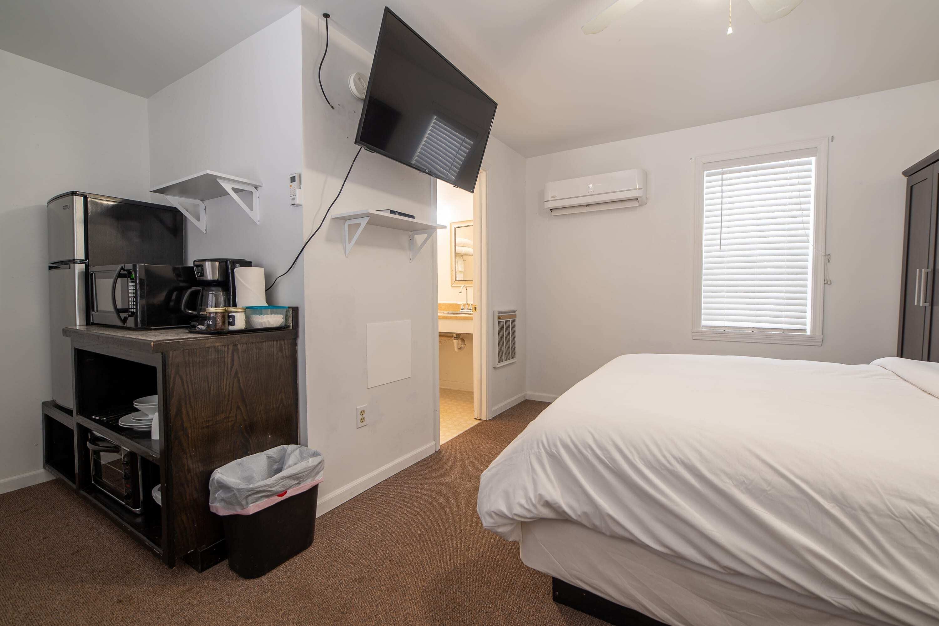 Ein Hotelzimmer mit Bett, einer Küchenzeile mit Mikrowelle, einer Kaffeemaschine und einem an der Wand montierten Fernseher.