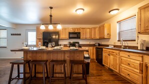 A spacious kitchen with wooden cabinets, a central island with stools, and modern appliances. - House at Inland Lakes Motel (Indian River)