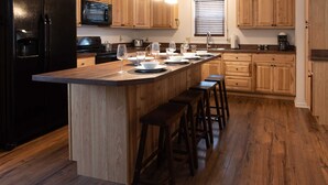 A kitchen with wooden cabinets, a black refrigerator, a microwave, and a large island with bar stools. - House at Inland Lakes Motel (Indian River)