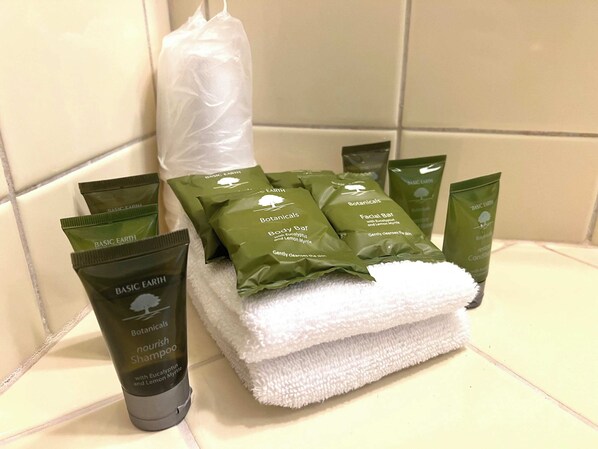 A bathroom with toiletries including a bottle of Basic Earth Nourish Shampoo, several green Botanical body bars, and a white towel.