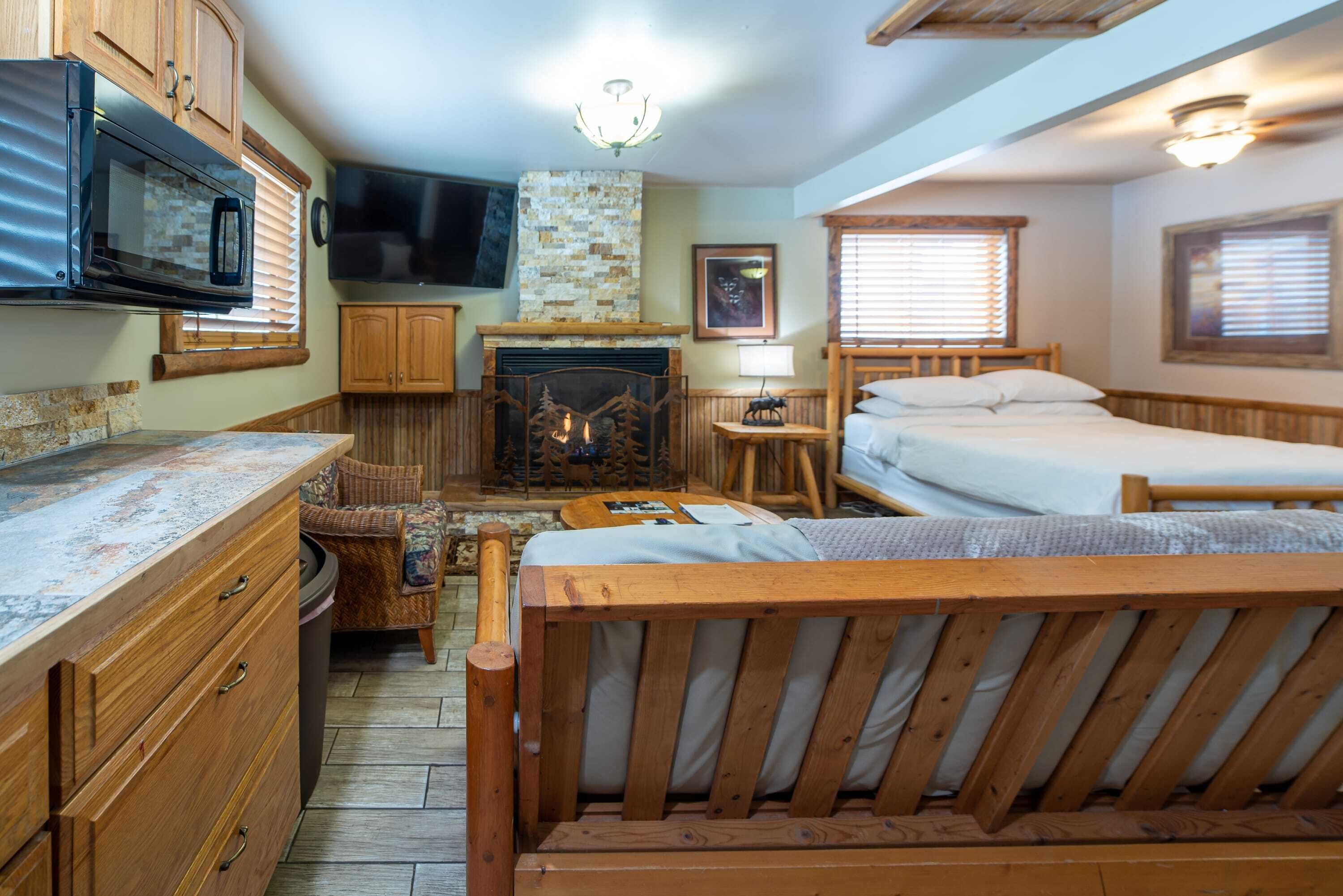 Una camera compatta con un letto di legno, un piccolo angolo salotto, un caminetto, un forno a microonde e una televisione.