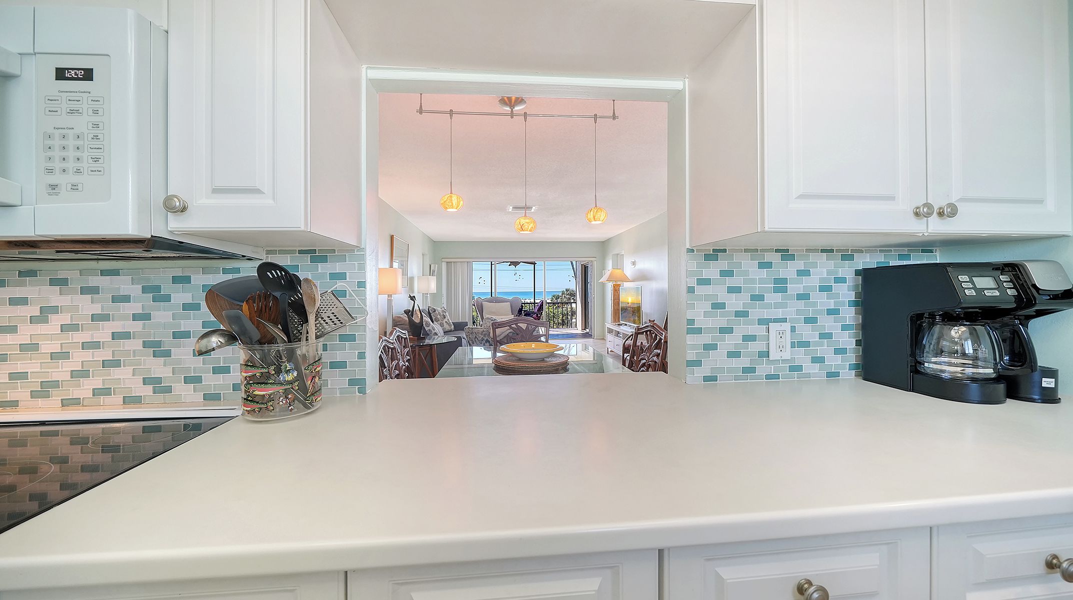 A modern kitchen with a microwave, coffee maker, and a dining area with a view of the ocean.