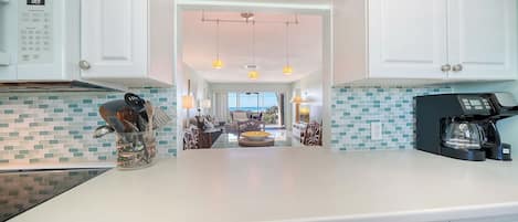 A modern kitchen with a microwave, coffee maker, and a dining area with a view of the ocean.
