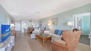 A spacious living room with a dining area, featuring a large TV, wicker furniture, and various decorative items.