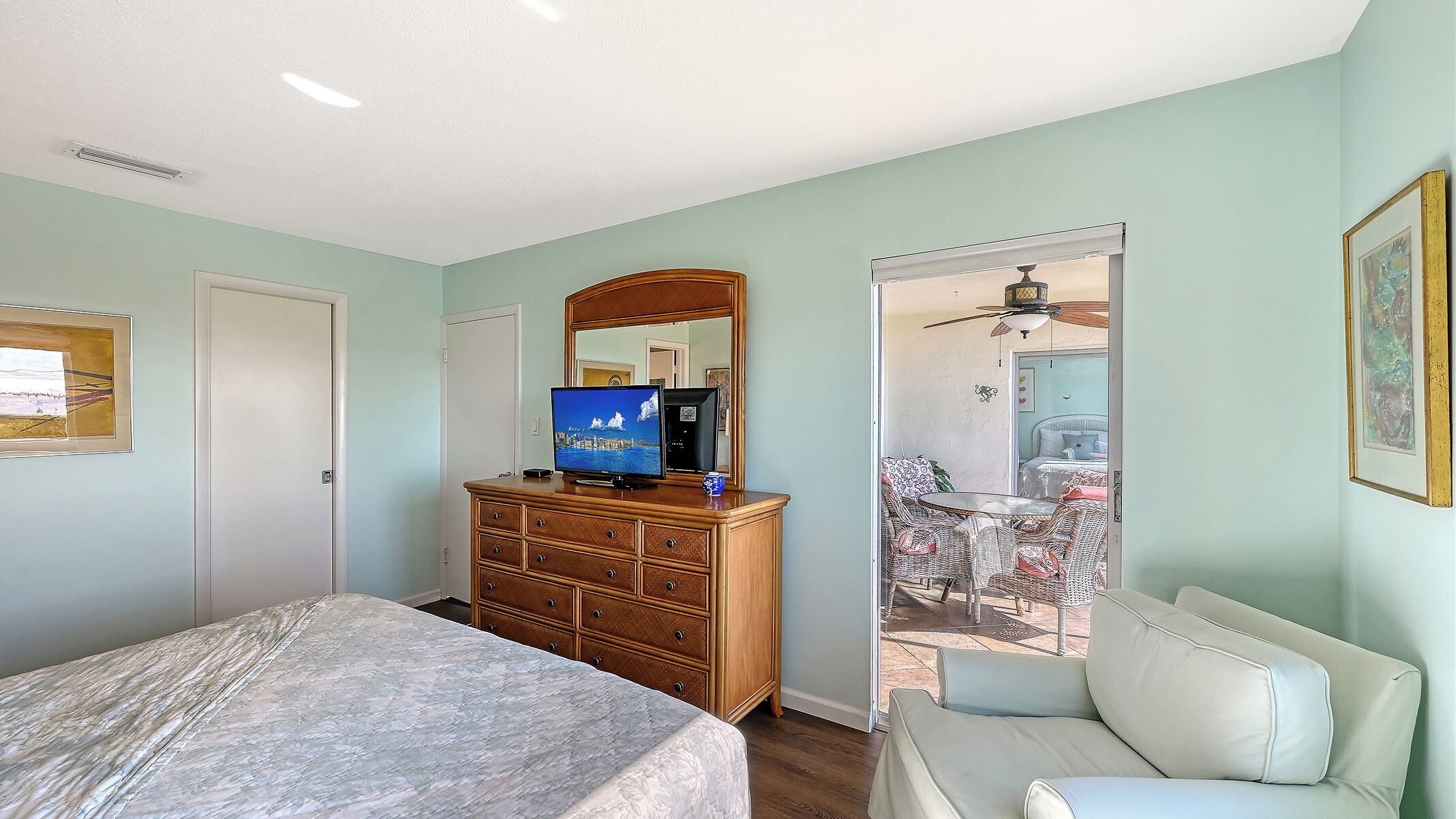 Ein Schlafzimmer mit Bett, Kommode, Fernseher und einem Balkon mit Sitzgelegenheit.