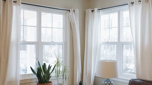 Un salón acogedor con un sofá de cuero marrón, un banco de madera con plantas en macetas y una mesita con una lámpara.