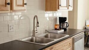 Una cocina con armarios de madera, encimera negra, fregaderos de acero inoxidable y una cafetera.