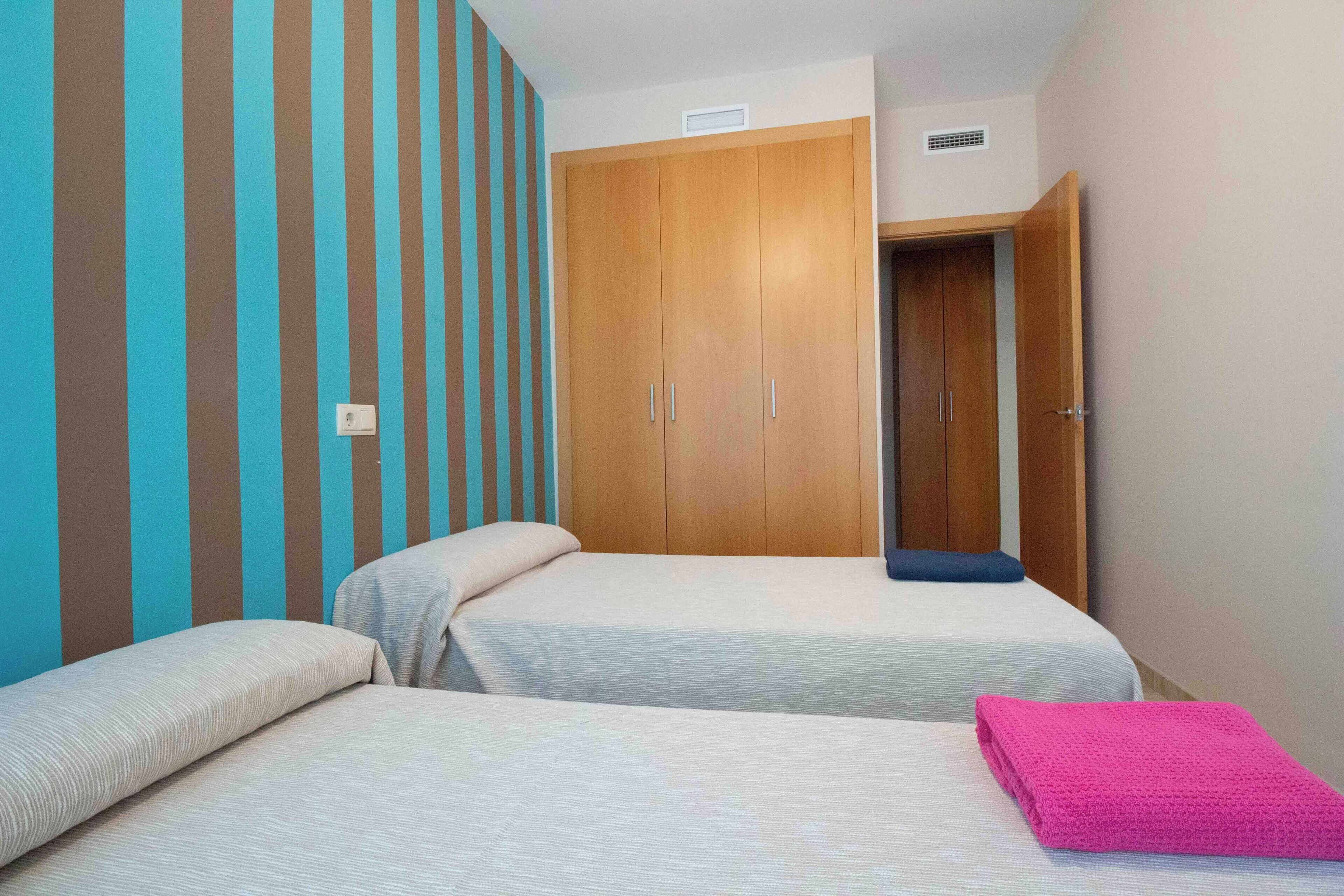 Una habitación con dos camas, un armario de madera y una pared a rayas.