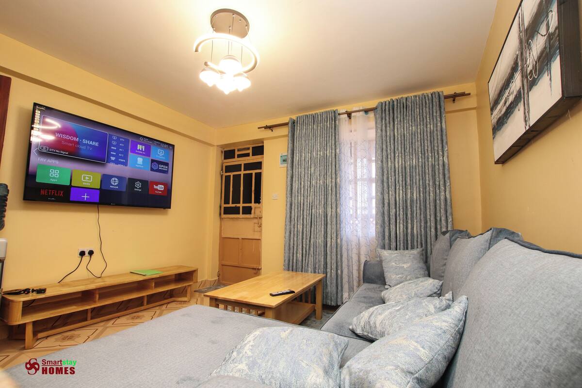 A living room with a flat-screen TV mounted on the wall, a wooden bench, a sofa, and a table.