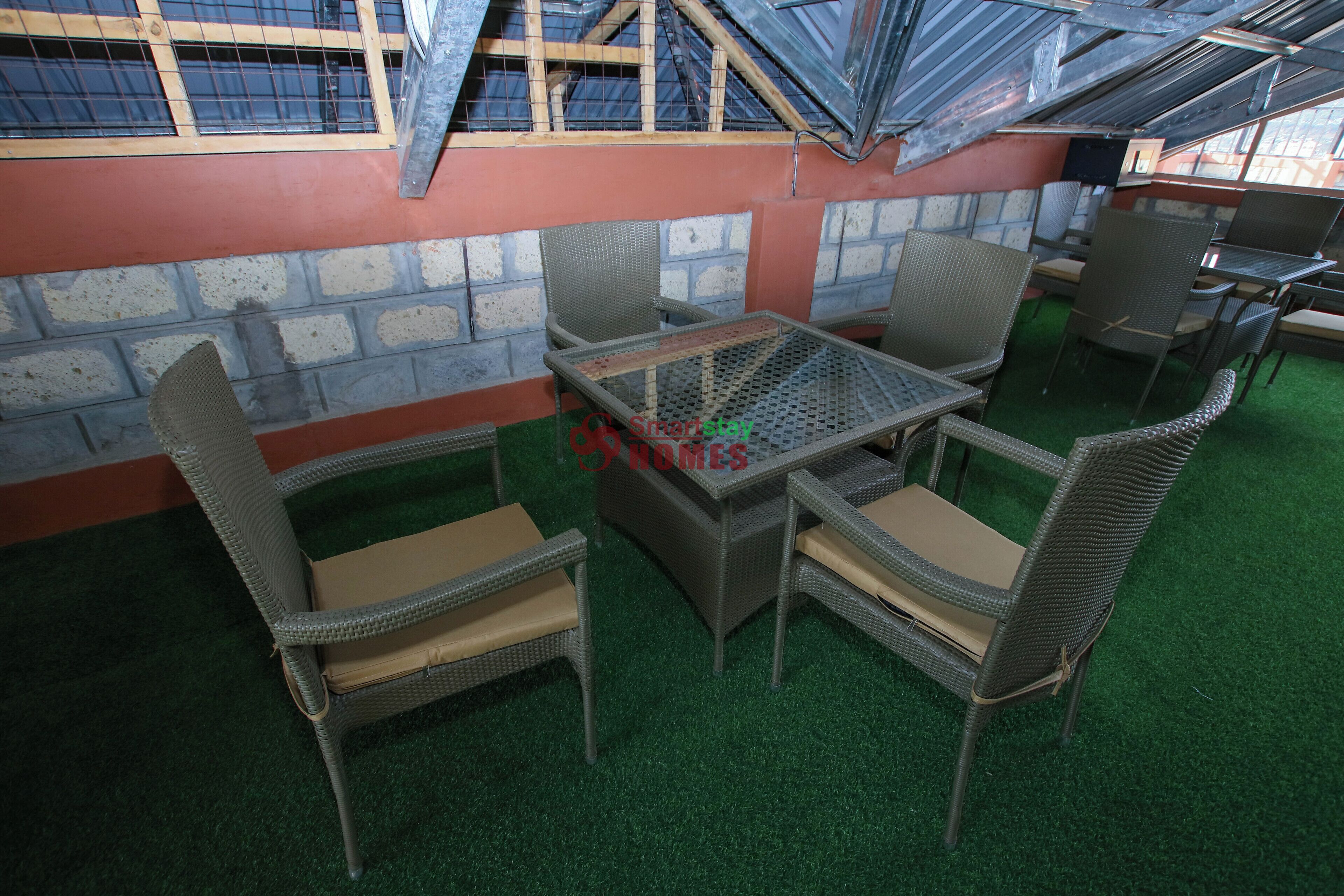 An outdoor seating area with wicker furniture and a glass-top table, surrounded by a brick wall and a green artificial turf floor.