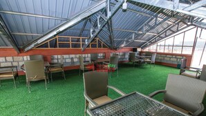 A rooftop terrace with a glass ceiling, green artificial turf, wicker furniture, and a view of the cityscape. - SmartStay KAG (Naivasha)