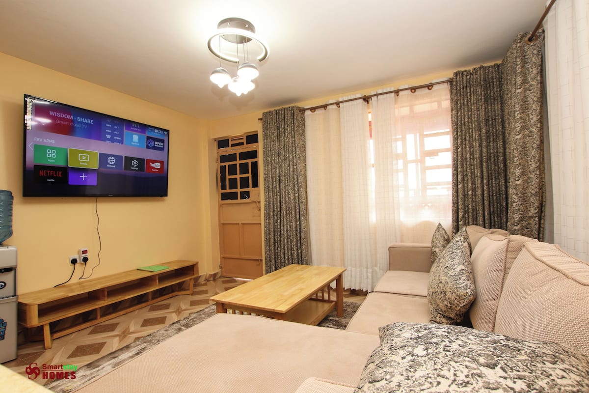 A living room with a flat-screen TV mounted on the wall, a wooden bench, a sofa, and a small table.