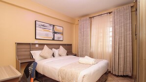 A hotel room with a bed, a nightstand, a wall-mounted artwork, and a window with curtains. - SmartStay KAG (Naivasha)