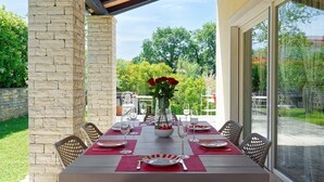 A dining area with a stone pillar, a table set for four with red placemats, and a vase with red flowers. - Villa Samanta - 6 Persons, 2 Bedrooms, Private Pool, Barbecue (Momjan)