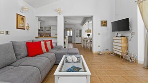 A modern living room with a grey sofa, red and white cushions, a glass coffee table with books, a TV, and a wooden dresser. - Villa Samanta - 6 Persons, 2 Bedrooms, Private Pool, Barbecue (Momjan)