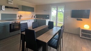 Eine moderne Küche mit Essbereich, ausgestattet mit Backofen, Geschirrspüler und einem an der Wand befestigten Fernseher.