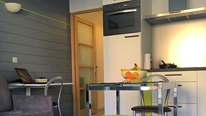 Une cuisine compacte dotée d’un four encastré, une table à manger avec deux chaises et un ordinateur portable posé sur un bureau.