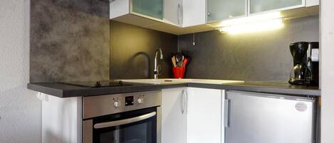 Eine kompakte Küche mit integriertem Backofen, einem kleinen Kühlschrank und einem Spülbecken.