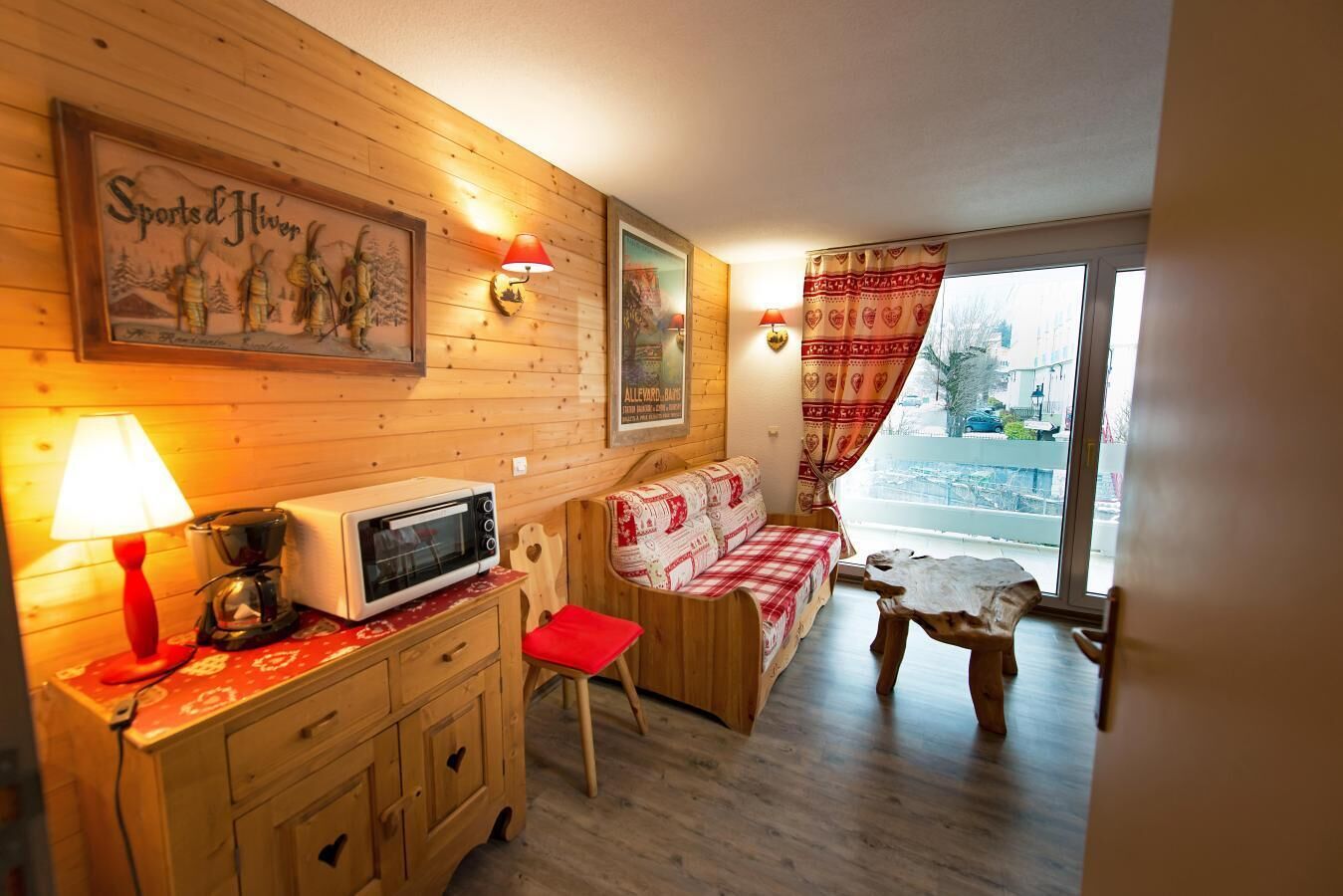 A cozy room with wooden walls, a red and white checkered sofa, a small wooden table, a microwave, and a red lamp.