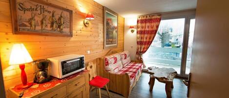A cozy room with wooden walls, a red and white checkered sofa, a small wooden table, a microwave, and a red lamp.