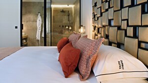 Una habitación de hotel moderna con una cama grande, zona de ducha con mampara de cristal y pared con estampado.