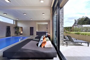 Uma área de piscina interior moderna com espreguiçadeiras e uma grande janela com vista para um jardim.