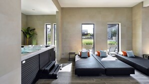 Un spa moderno con jacuzzi, una cama grande con almohadas y vistas al exterior a través de amplios ventanales.