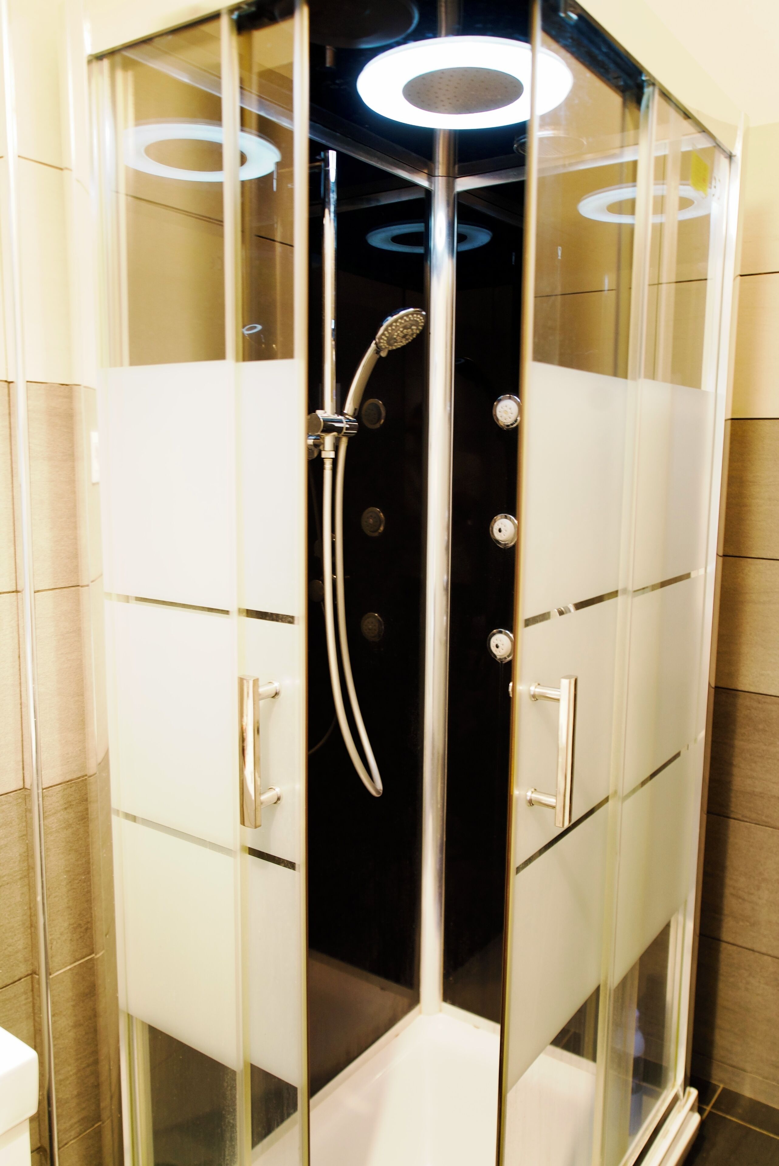 A modern glass-enclosed shower with a handheld showerhead and a wall-mounted faucet.