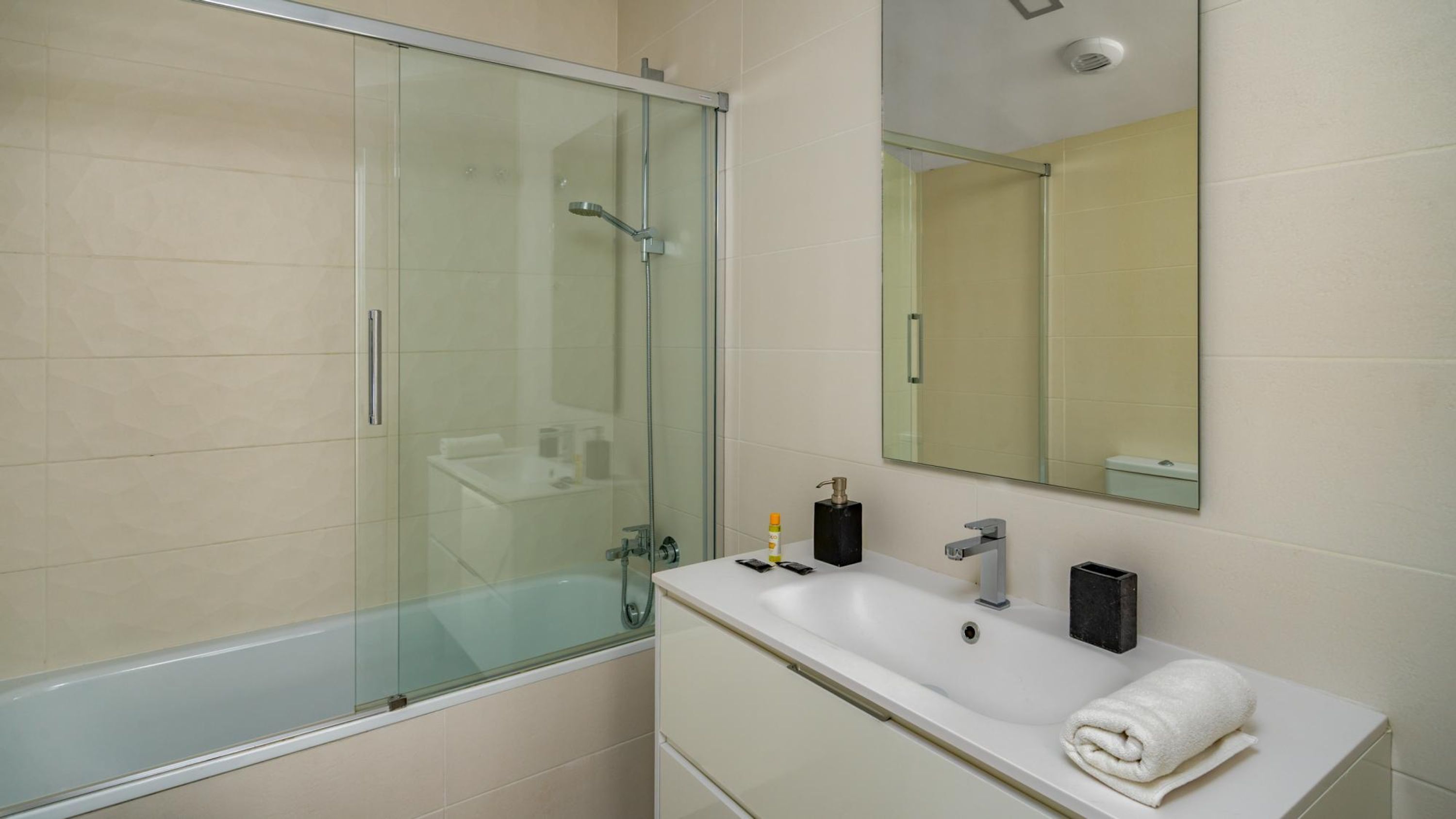 A modern bathroom with a glass-enclosed shower, a white sink, and a mirror above it.