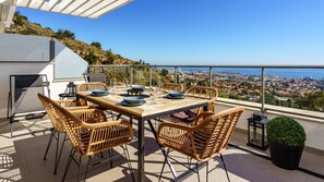 A dining area with a table set for four, surrounded by wicker chairs, overlooking a cityscape. - Top-floor Apartment With Pool Ref 20 (Benalmádena)