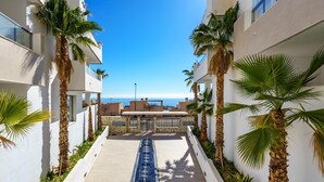A corridor with a view of the sea, flanked by palm trees and modern buildings. - Top-floor Apartment With Pool Ref 20 (Benalmádena)