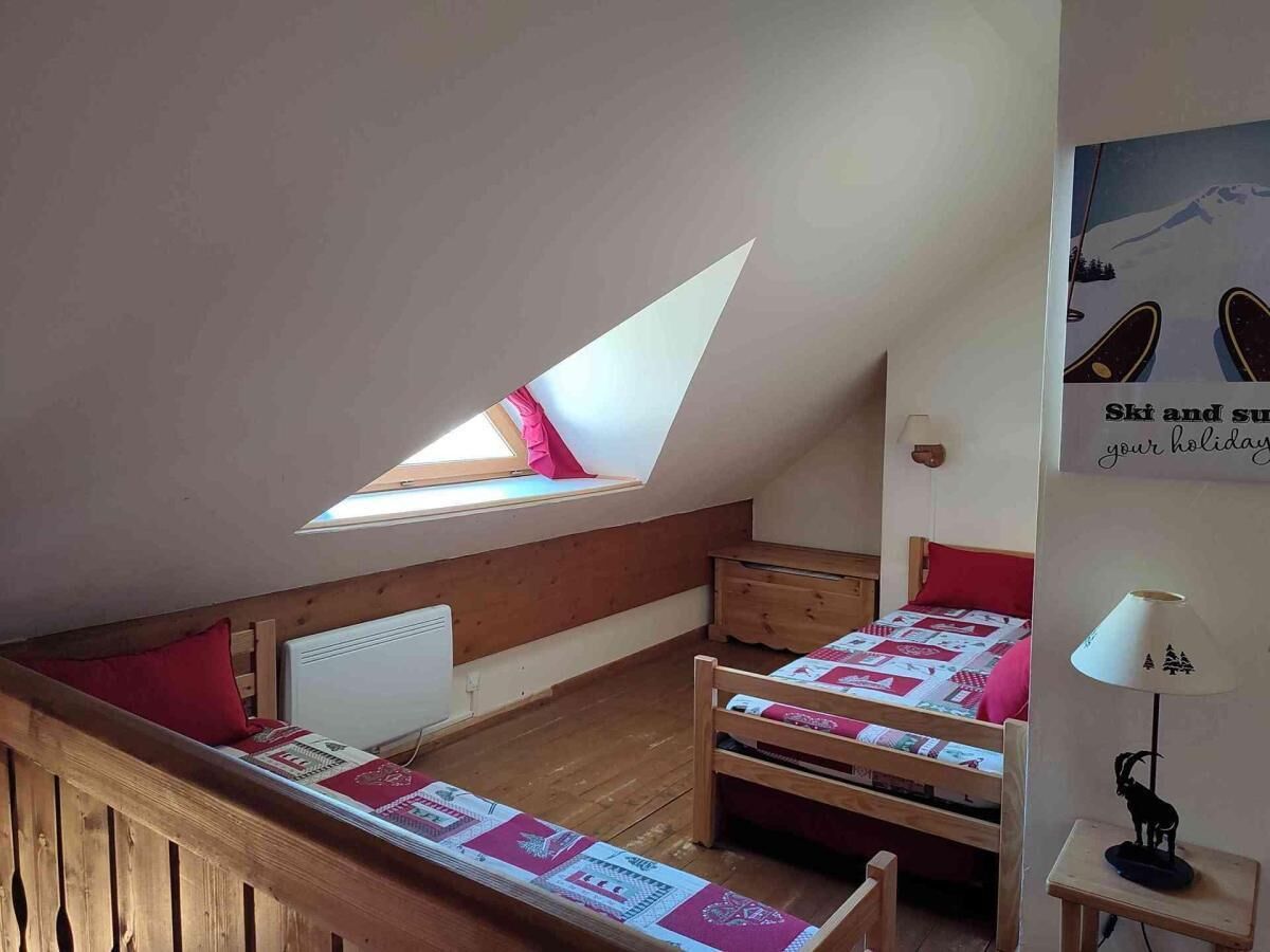 Une chambre confortable située sous les toits, avec un plafond en pente, deux lits en bois, une lucarne et une lampe fixée au mur.