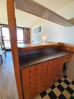 Una cocina compacta con armarios de madera, encimera de acero inoxidable y suelo a cuadros.