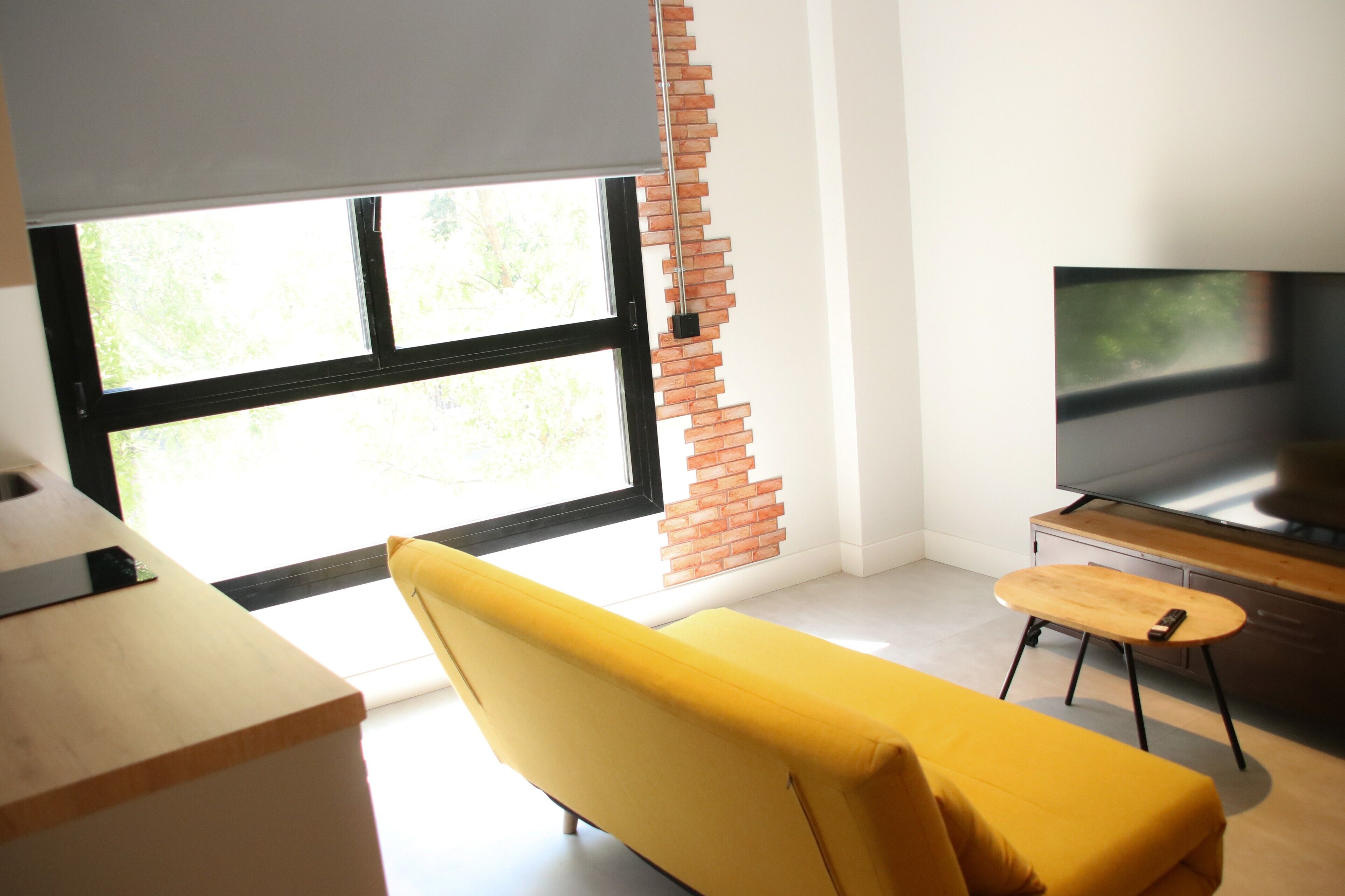 Un soggiorno moderno con un divano giallo, una TV e un decoro murale in mattoni.