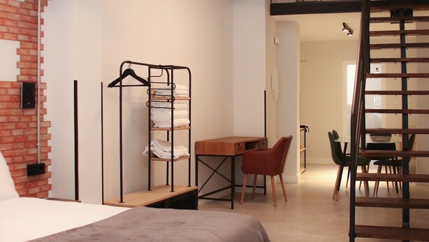 A modern room with a bed, a desk, and a chair. There is a hanging light fixture and a brick wall. - Loft Imperial (Madrid)