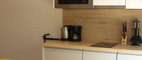 Cocina compacta con microondas, cafetera y utensilios sobre la encimera.