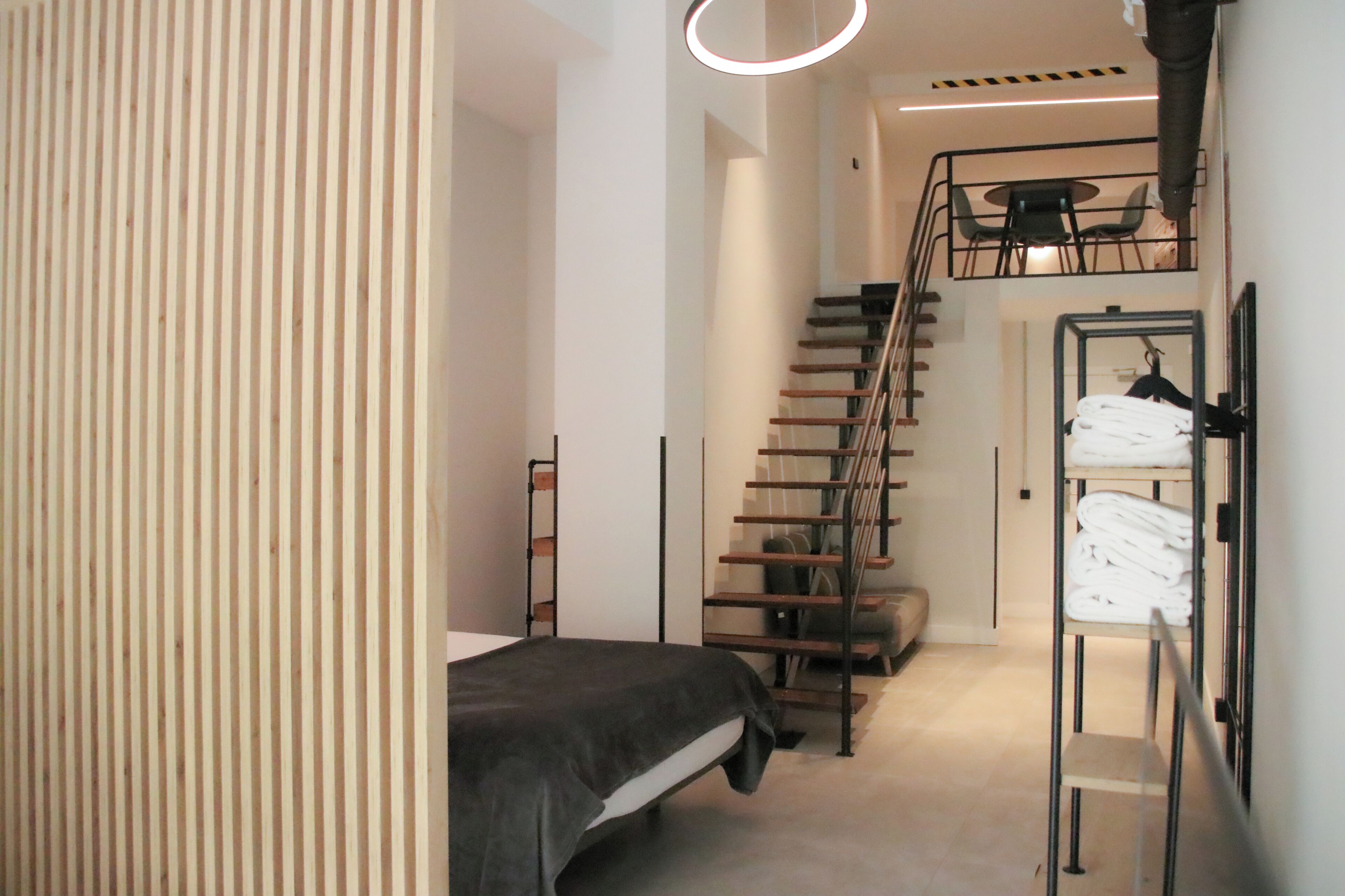 Een moderne slaapkamer met een bed, een trap en een rek met opgevouwen handdoeken.
