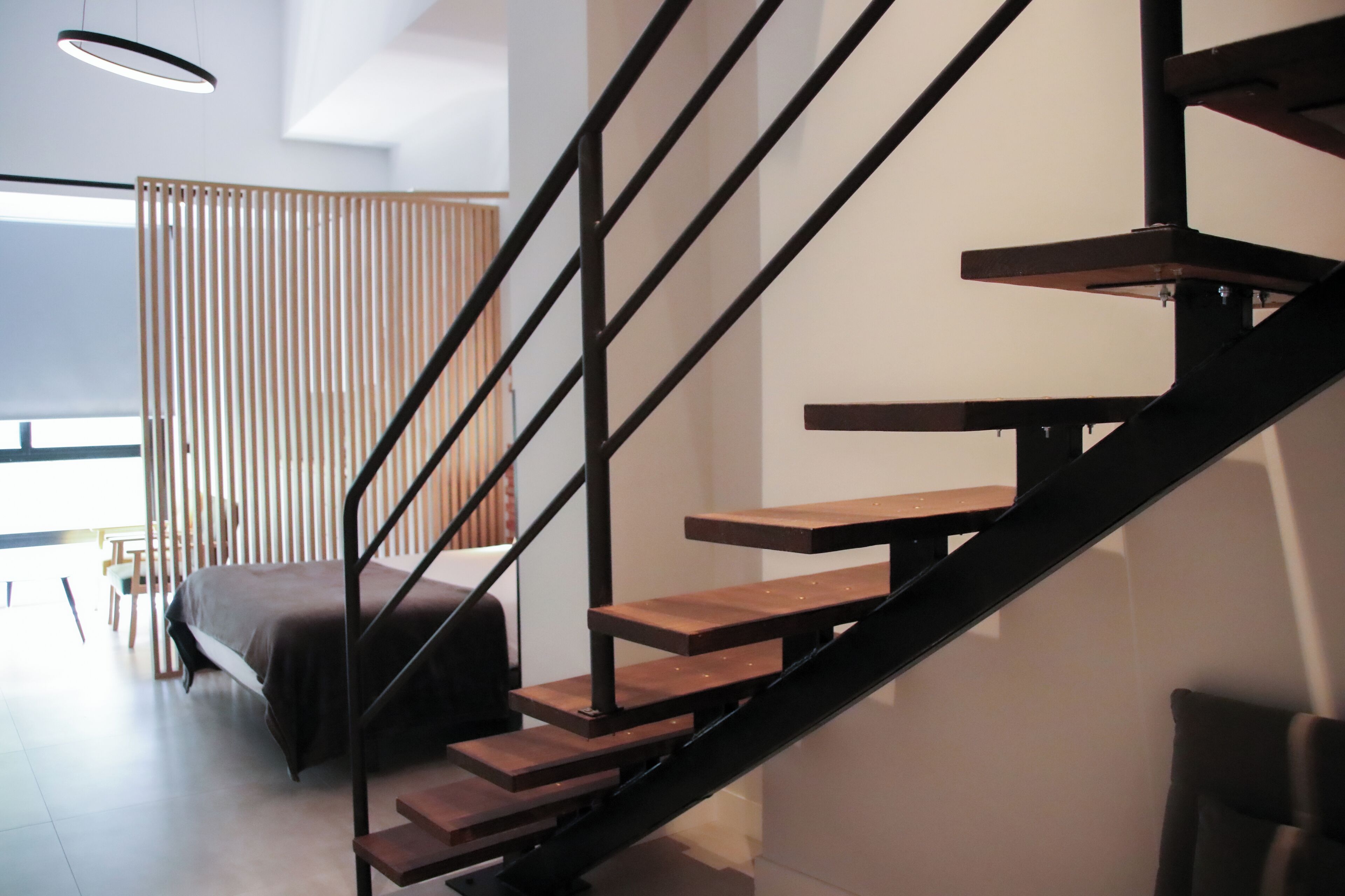 Un interior moderno con una escalera de madera, una cama y una habitación con un gran ventanal.