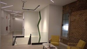 A modern interior with a staircase, a glass wall with a green accent, a yellow armchair, and a wooden chair. - Loft Imperial (Madrid)