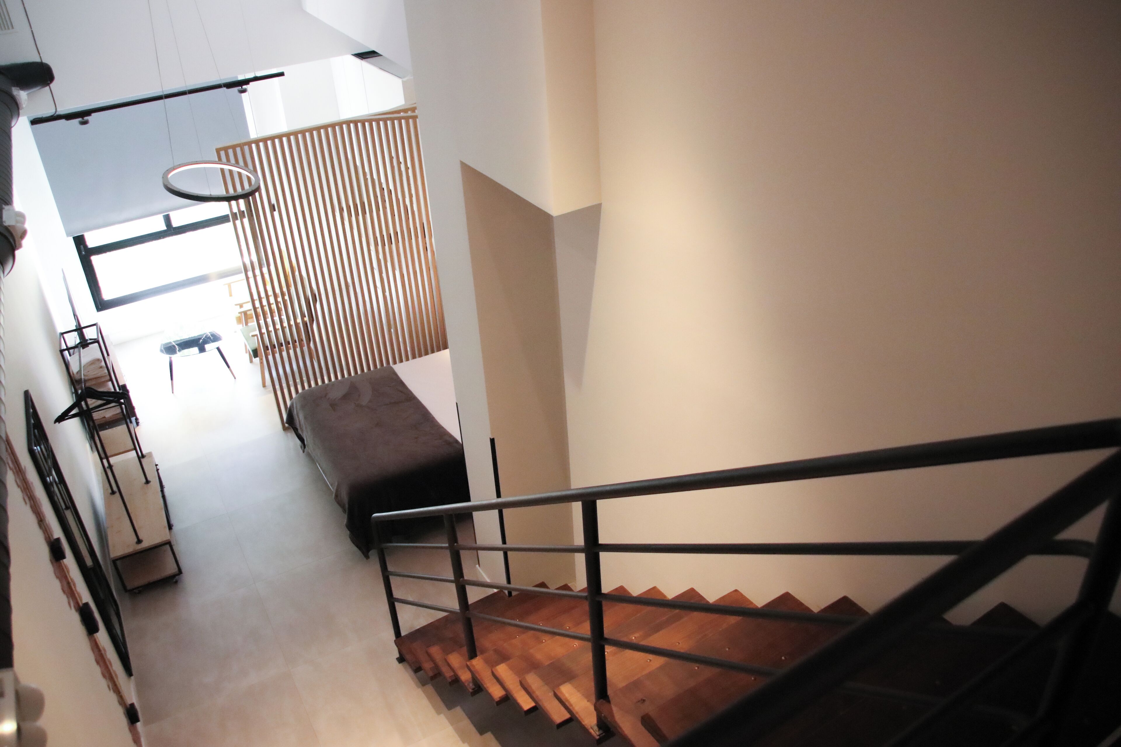 Una escalera moderna con detalles de madera y barandilla de metal, que conduce a un espacio con un banco y una lámpara colgante.