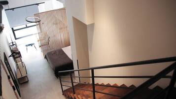 Una escalera moderna con detalles de madera y barandilla de metal, que conduce a un espacio con un banco y una lámpara colgante.