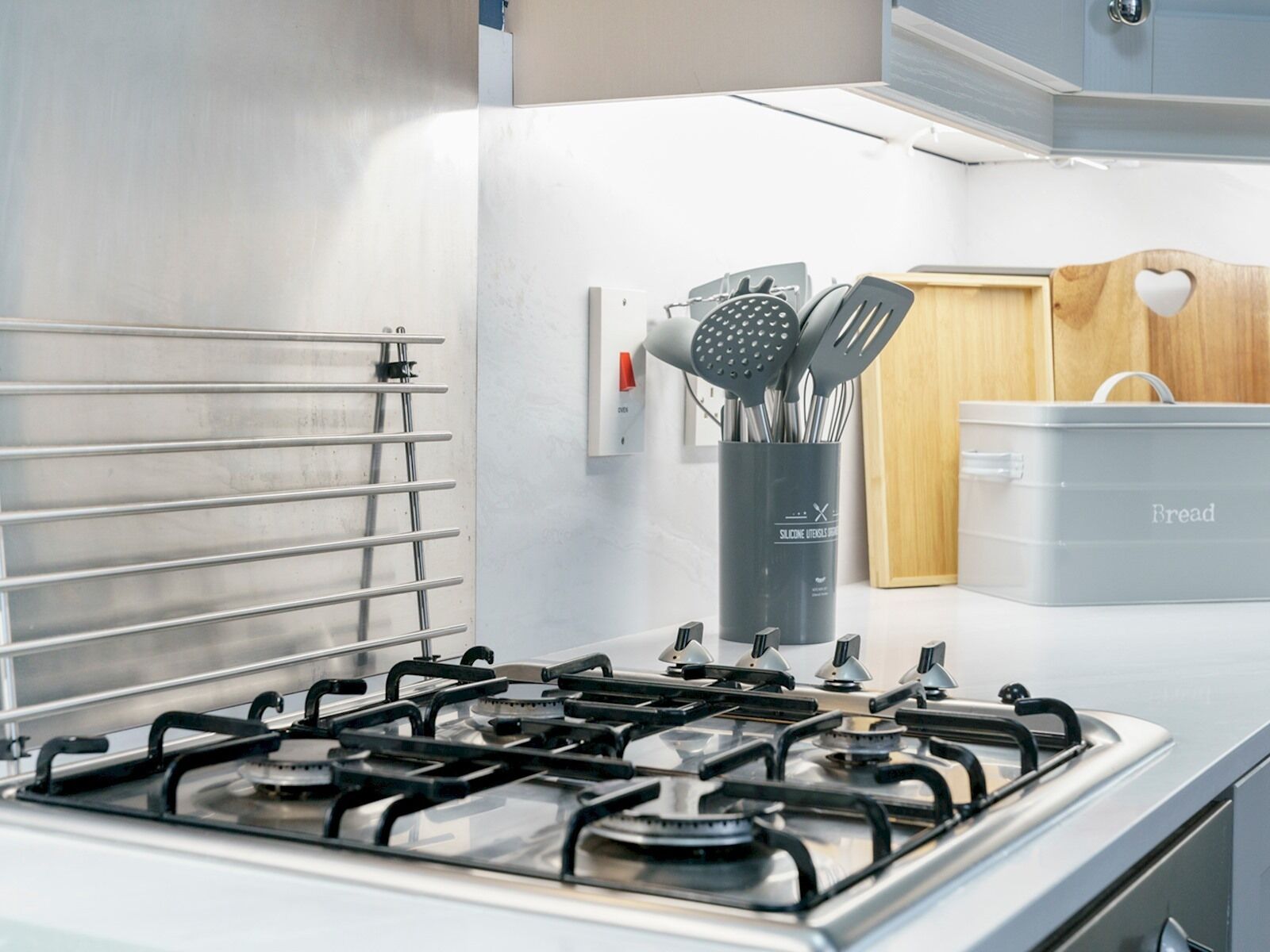 A kitchen with a gas stove, a stainless steel range hood, and a silicone utensil holder.