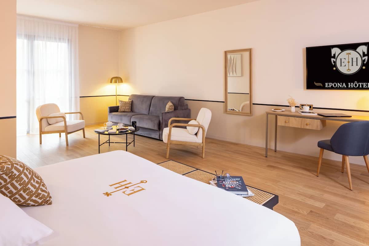 Ein Hotelzimmer mit einem Bett, zwei Sesseln, einem Sofa, einem Schreibtisch und einer Lampe.