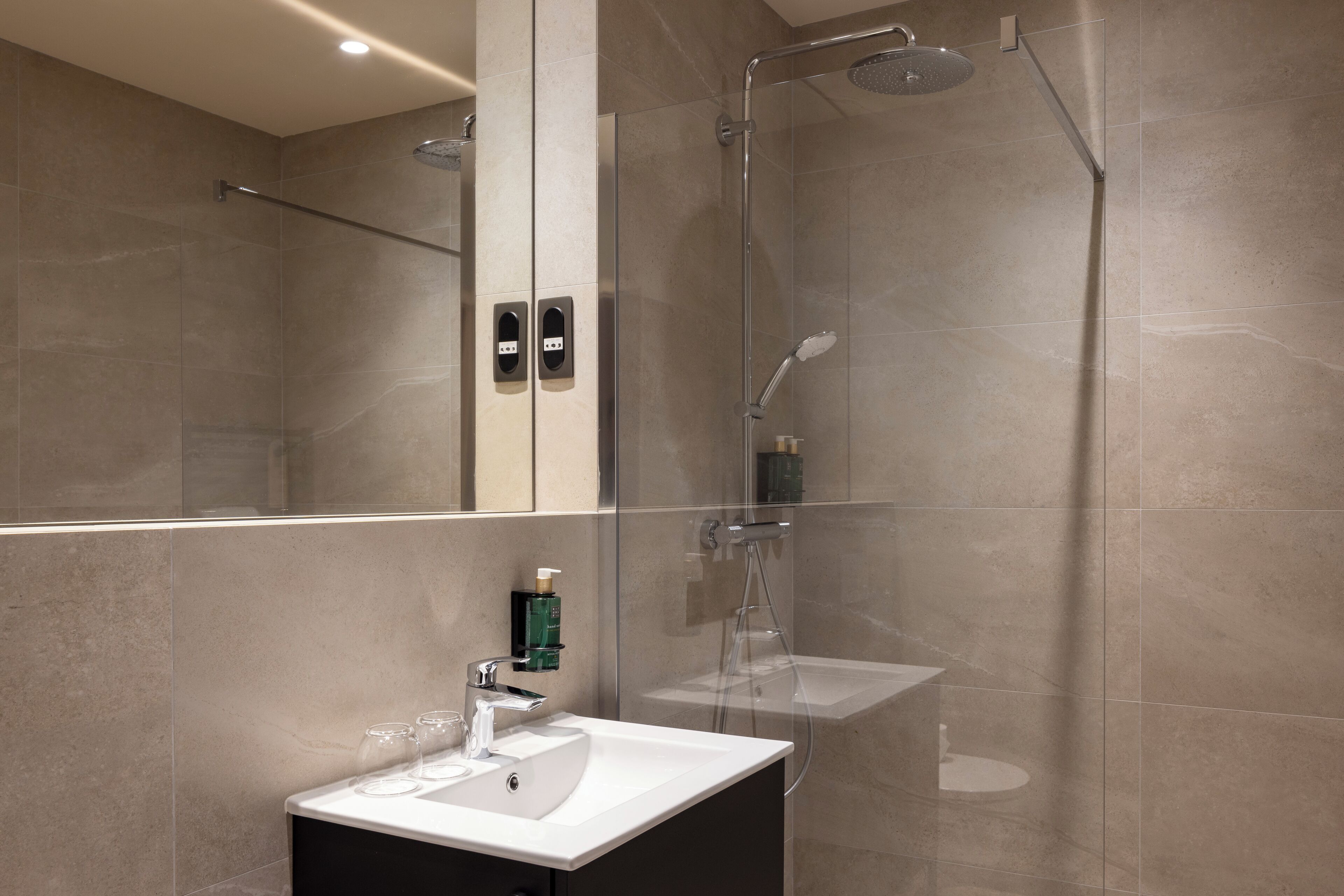 A modern bathroom with a glass-enclosed shower, a white sink, and a mirror.